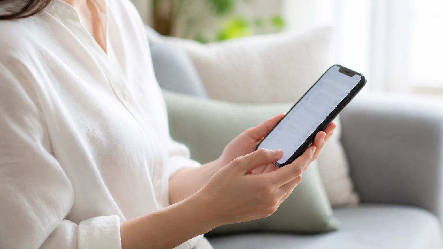 自宅のソファでスマートフォンの設定を確認する女性の手元