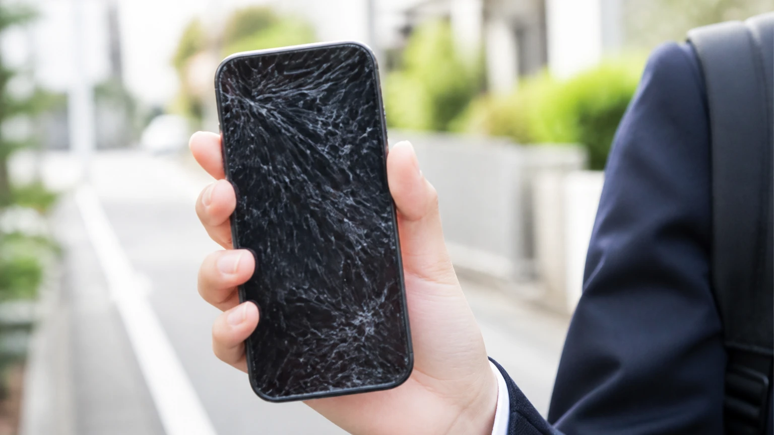 画面にひびが入ったスマートフォンを持つ学生の手元