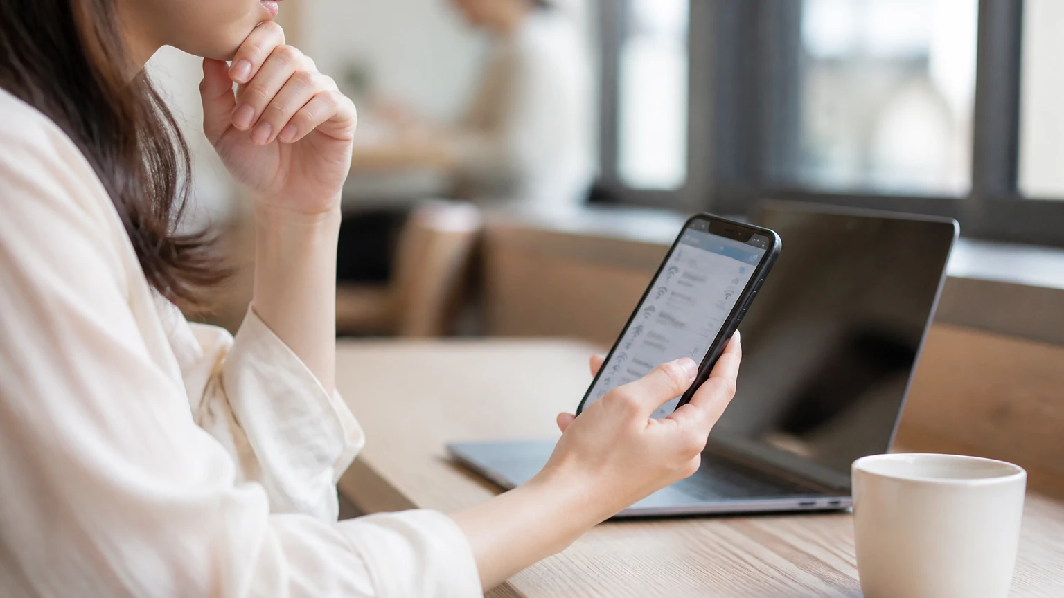 カフェでスマートフォンのWi-Fi一覧を見ながら接続先を考える女性