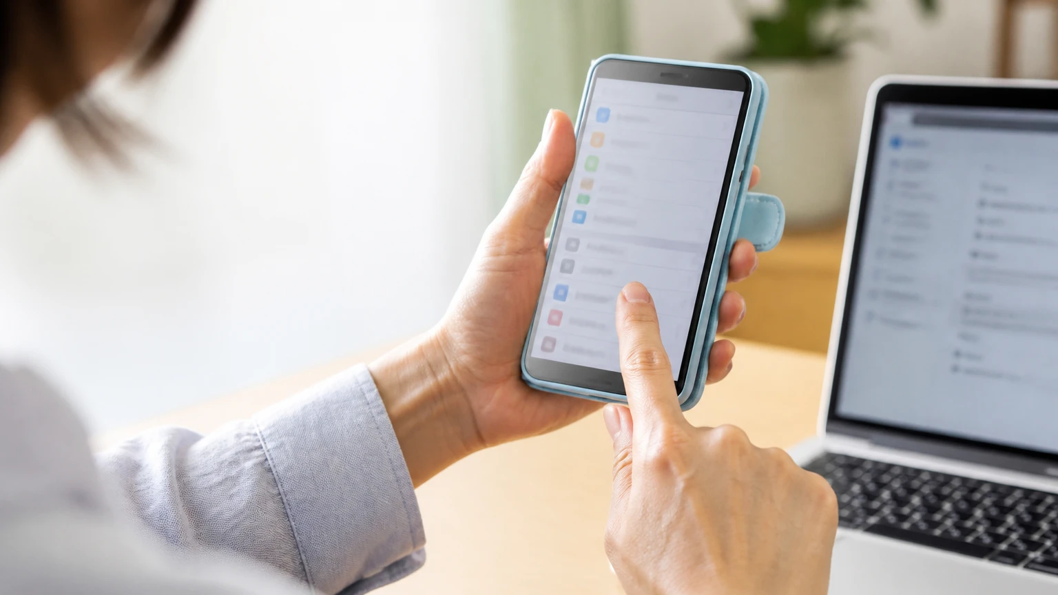 パソコンを横にして子どものスマートフォンの設定を変える保護者の手元
